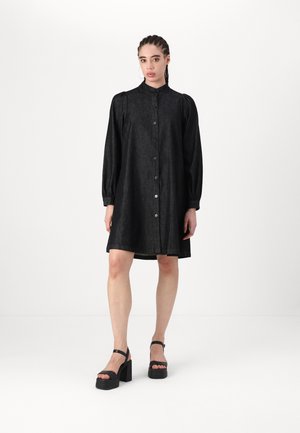 Black denim shirt dress with long puff sleeves, button front closure, and relaxed fit. Paired with chunky black platform sandals.