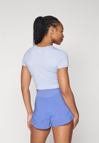 Camicia azzurra chiara a maniche corte aderente e pantaloni sportivi viola. La camicia presenta un colletto rotondo; i pantaloni hanno una vita larga e un orlo curvo.