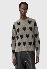 Maglione grigio morbido con motivi a cuore neri, collo rotondo e maniche lunghe. Abbinato a pantaloni di pelle neri. Texture soffice.