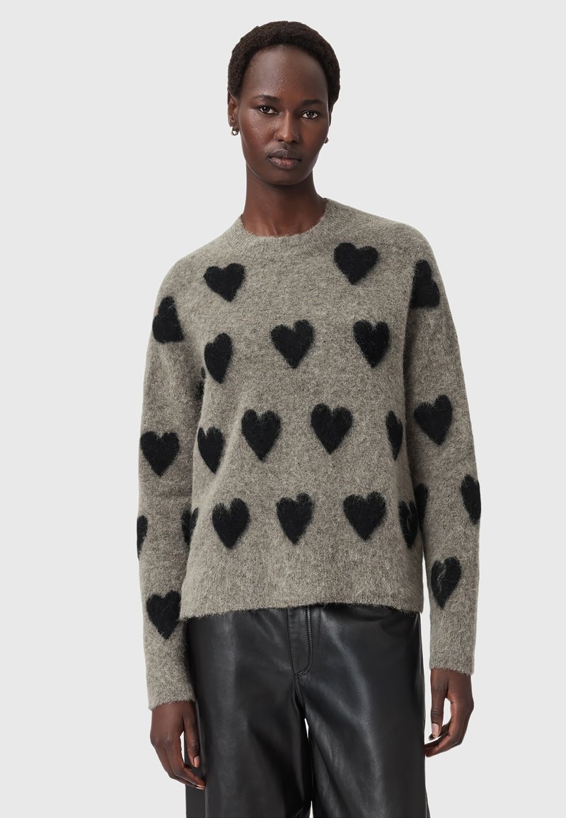 Maglione grigio morbido con motivi a cuore neri, collo rotondo e maniche lunghe. Abbinato a pantaloni di pelle neri. Texture soffice.