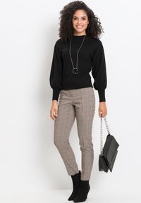 Maglione nero a maglia con maniche a sbuffo, abbinato a pantaloni a quadri rossi e beige, e stivaletti neri con tacco. Gli accessori includono una collana argentata e una borsa nera.