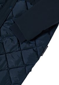 Giacca trapuntata navy con maniche a coste, caratterizzata da una texture liscia e una finitura lucida. Include un'etichetta del marchio sul lato.