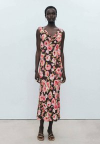 Rochie florală cu decolteu tip cowl, fabrică întunecată cu flori mari roz și verzi, până la genunchi, completată de sandale simple maro.