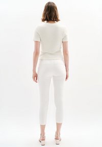 Top blanco texturizado de manga corta combinado con pantalones cortos ajustados blancos. La modelo lleva tacones de color claro y una sencilla cadena como collar.