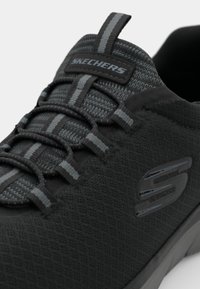 Melna sporta kurpe, izgatavota no teksturēta sieta auduma ar iepresētu zoli. Iezīmēta ar pelēkiem akcentiem, elastīgām šņorēm un Skechers logo sānos.