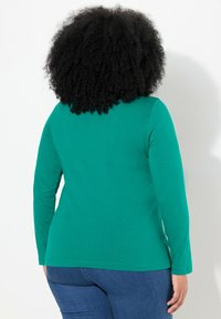 Langarmige groene T-shirt van zachte stof, met een ronde halslijn en een aansluitende silhouet, gecombineerd met blauwe jeans.