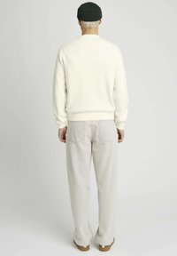 Sweatshirt crème avec des poignets côtelés, associé à un pantalon gris clair avec des poches arrière, vu de dos. Un bonnet vert foncé complète le look.