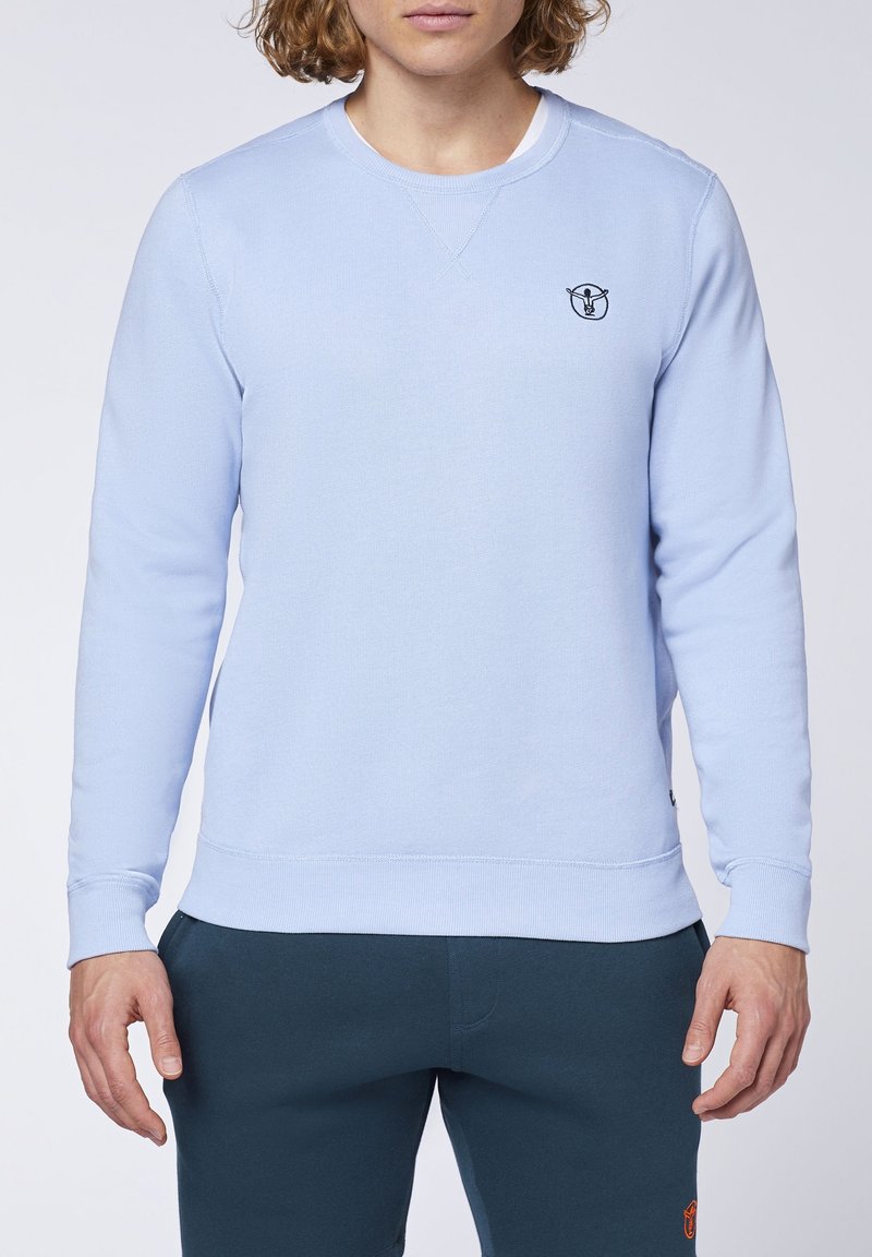 Světle modrý sweatshirt s kulatým výstřihem, vyrobený z měkké bavlny, se žebrovanými manžetami a lemem, s malým černým logem na hrudi.