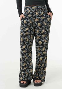 Pantalons fluides noirs à fleurs avec un mélange de fleurs jaunes, bleues et blanches. Ils offrent une coupe décontractée et des poches latérales pour plus de fonctionnalité.