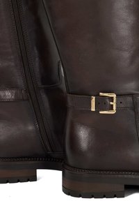Bruine leren enkellaarzen hebben een zijrits, een gouden gesp detail bij de enkel en een gestructureerde zool met een licht verhoogde rand.
