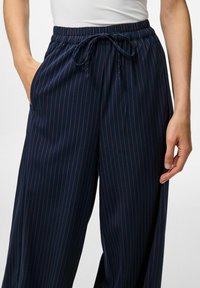 Jūras zilās svītrainās bikses, kas izgatavotas no viegla auduma, ar elastīgu jostu un auklu, kā arī sānu kabatām.