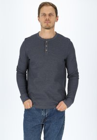 Långärmad, mörkgrå henleytröja med rund halsringning, tre träknappar och textilstruktur; tillsammans med blå denimjeans.