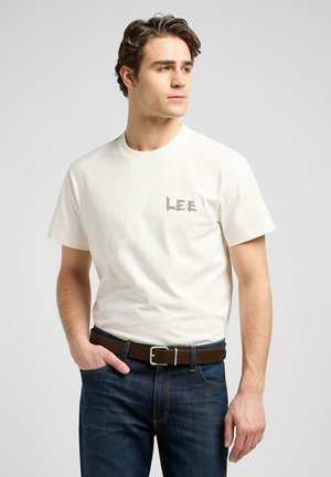 Weißes Baumwoll-T-Shirt mit grauem "LEE"-Logo auf der Brust, kombiniert mit dunkelblauen Jeans und einem braunen Gürtel. Einfaches Rundhalsausschnitt-Design.