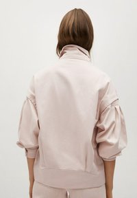 Jasnoróżowy sweter z wysokim kołnierzem, bufkami na rękawach i elastycznymi mankietami. Miękka tkanina, luźny krój i minimalistyczny design.