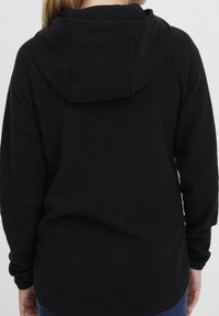 Sweat-shirt à capuche noir avec une texture douce, des manches longues et une coupe décontractée. Il présente un ourlet arrondi et une capuche prononcée.