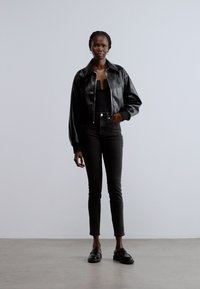 Chaqueta corta de cuero negro, top ajustado negro, jeans negros ajustados y mocasines negros. Textura suave, diseño estructurado y paleta monocromática.