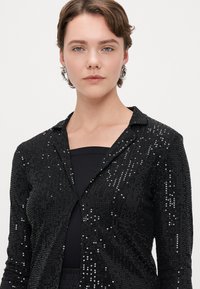 Czarna koszula zapinana na guziki z cekinami, z kołnierzykiem, o teksturowanej powierzchni, długich rękawach i dopasowanym kroju.