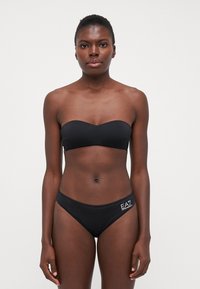 Crni bandeau bikini gornji dio s glatkom teksturom i odgovarajući donji dio s niskim strukom sa malim bijelim logotipom sa strane.