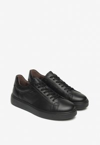 Sneakers in pelle nera con chiusura con lacci, punta arrotondata e dettagli testurizzati. Presenta una suola in gomma e un morbido rivestimento interno marrone.