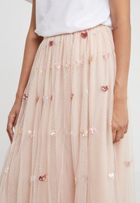 Vrouw in een lichtroze tule rok met pailletten hartversieringen en een ingestopt wit topje, met haar handen naast zich.