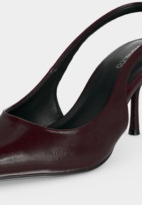 Chaussure à talon haut slingback en cuir rouge foncé avec bout pointu et talon fin sur un fond uni.