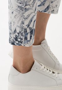 Baskets blanches à finition texturée, associées à un pantalon court imprimé de feuillages bleus et gris. Coutures apparentes et revers.