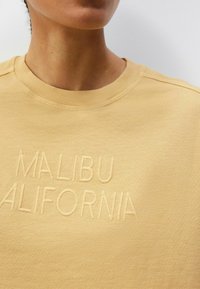 Žlutá mikina s výšivkou textu "MALIBU CALIFORNIA", s kulatým výstřihem a texturovanou, měkkou tkaninou.