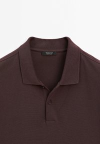 Ciemnoczerwona koszulka polo z klasycznym kołnierzykiem, zapięciem na dwa guziki i teksturowanym materiałem. Metka głosi "Massimo Dutti, wyprodukowano w Turcji."