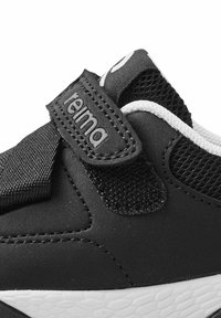 Czarne buty sportowe z syntetycznej górnej części, z siateczkowymi akcentami, regulowanym paskiem na rzep oraz białą fakturowaną gumową podeszwą.