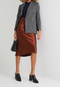 Blazer doppiopetto a scacchi grigi e neri, top blu navy, gonna in raso lucido color ruggine, mule nere con tacco e una piccola borsa nera.