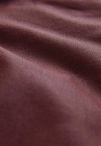 Burgundia värviga kangas, millel on sile, tekstuuriga pind ja kerge läige, millel on õrnad voldid, mis loovad erinevaid valguse peegeldusi.