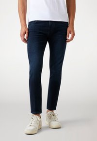 Tummansiniset farkut, jotka on valmistettu denimistä, slim fit -malli, viisi taskua ja hienovaraiset haalistumat. Yhdistetty valkoisiin lenkkareihin.