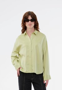 Ανοιχτό πράσινο, πουκάμισο με μακριά μανίκια και άνετη εφαρμογή, με γιακά και απαλό ύφασμα. Συνδυασμένο με σκούρα τζιν.