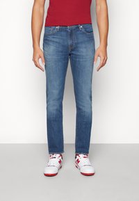 Blå denimjeans med rett passform, som har fem lommer, stikninger og lett falming. Kombinert med hvite og røde sneakers.