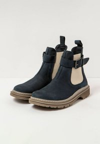 Botas de tobillo de cuero azul oscuro con paneles laterales elásticos beige, una correa con hebilla y una suela de goma texturizada. Acabado suave con detalles de costura.