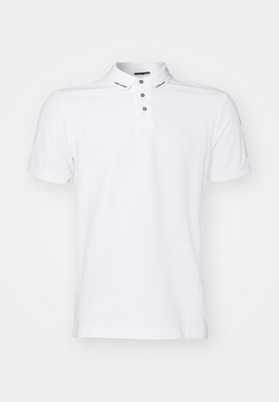 Chemise polo blanche à manches courtes et col boutonné. Présente des boutons gris et des détails de marque au niveau du col. Texture de tissu lisse.
