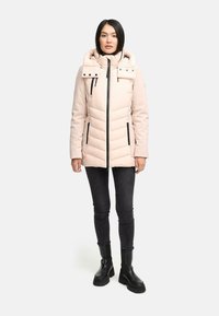 Ljusrosa puffjacka med hög krage, dragkedjestängning och horisontell sömnad. Har svarta dragkedjor och detaljer. Kombinerad med svarta tajta jeans och stövlar.