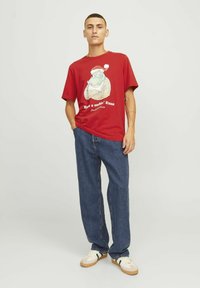 Rød bomulds t-shirt med et julemand grafik med tatoveringer og teksten "Have a rockin' Xmas." Båret med blå denim jeans og creme sneakers.