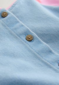 Gros plan sur un tissu denim bleu clair avec des boutons marron à quatre trous cousus le long d'une couture.
