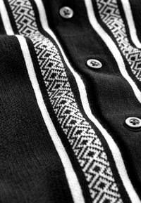 Tissu noir à boutons avec des rayures verticales blanches à motifs géométriques et des lignes blanches unies de chaque côté.