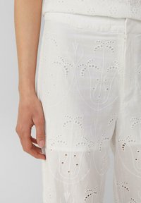 Weiße bestickte Hosen mit floralen Mustern und Cut-out-Details sowie einer glatten Textur. Der Stoff ist leicht und luftig.