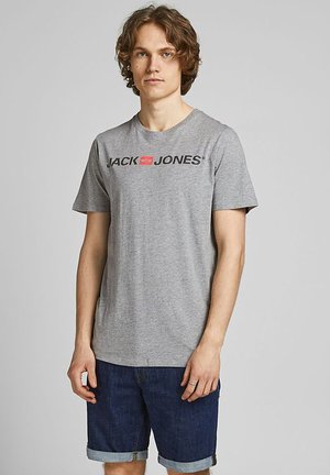 Graues Baumwoll-T-Shirt mit kurzen Ärmeln, versehen mit einem schwarzen und roten "JACK & JONES"-Logo auf der Brust. Trägt dazu eine Jeansshorts.