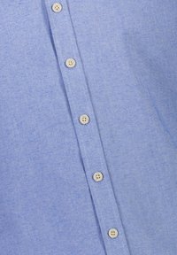 Vaaleansininen paita, jossa on tekstuurikangas, pystysuora napitus, jossa on kuusi kermaista nappia, sekä sileä ja hieman heatheroitunut viimeistely.