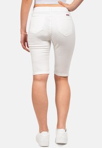 Shorts en denim blanc au design ajusté, avec des ourlets retournés et deux poches arrière. Portés avec des baskets blanches sur un fond clair.