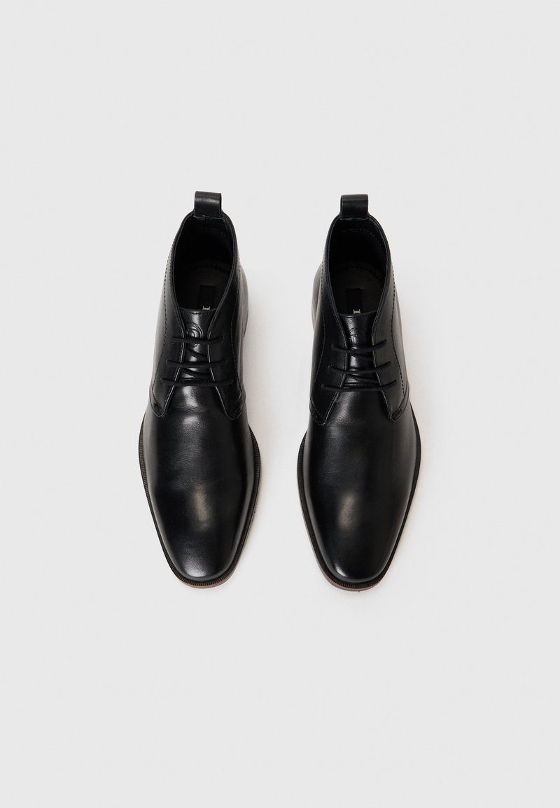 Para polerowanych czarnych skórzanych botków za kostkę na sznurówki z pętlami do zakupu, widzianych z góry na białym tle.