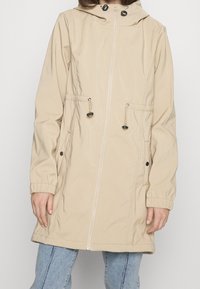 Beige voděodolná bunda s kapucí na stahování, zipem vpředu, elastickými manžetami a dvěma bočními kapsami. Hladká textura a lehký design.