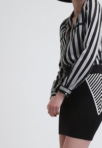 Camicia a righe verticali bianco e nero con scollatura profonda, abbinata a una gonna nera aderente con accenti geometrici bianchi.
