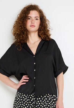 Camicia nera a maniche corte con chiusura a bottoni e vestibilità rilassata. Tessuto liscio, orlo leggermente curvato e colletto a punte. I bottoni sono di colore chiaro.