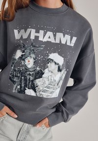 Grauer Sweatshirt mit einem grafischen Aufdruck von zwei Figuren in Winterkleidung mit Schneeflocken, beschriftet mit "WHAM!" in fetten weißen Buchstaben.
