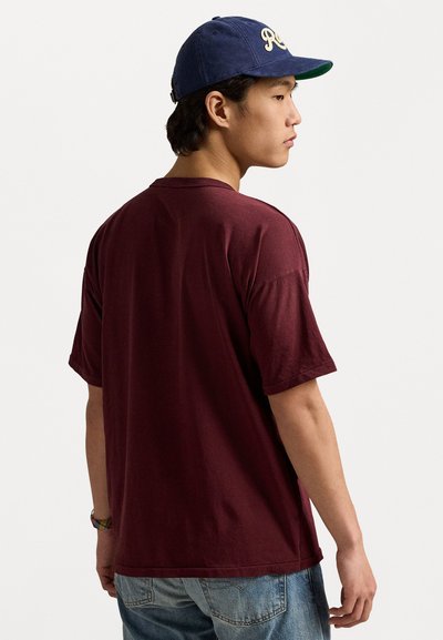 Bordeaux katoenen t-shirt met korte mouwen en een ronde hals, gecombineerd met lichtblauwe denim jeans en een marineblauw pet met witte letters.